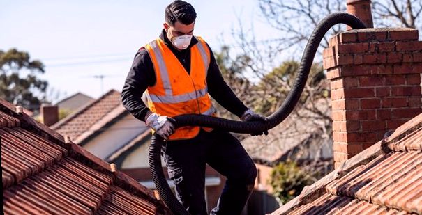 Technician carrying a long flexible line across a tiled roof to the chimney